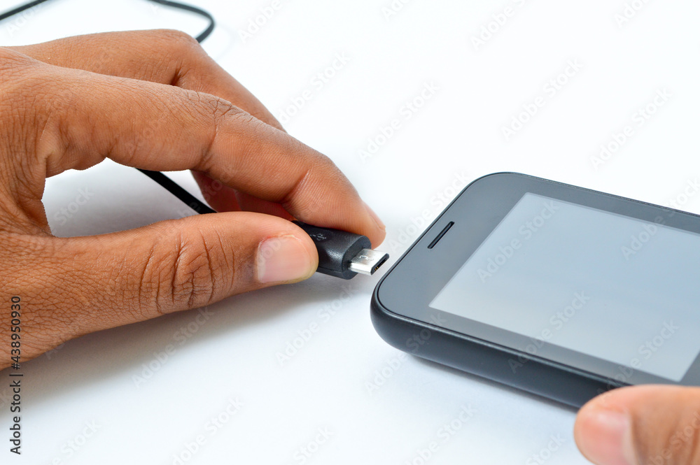 Charging a smartphone via a USB cable and a power supply on a white background. Silhouette of a black smartphone hanging with a usb charging cable on a white background Charging a smartphone via a USB cable and a power supply on a white background. Silhouette of a black smartphone hanging with a usb charging cable on a white background
