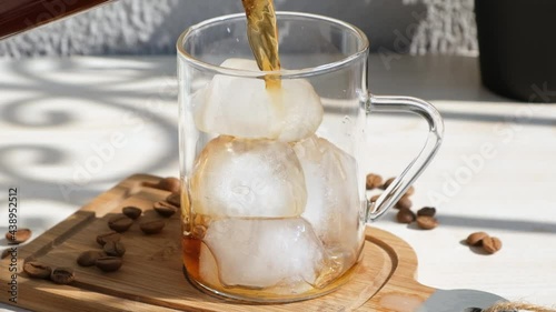 pouring brewing filter coffee into glass full of ice. Making cold coffee in slow motion.