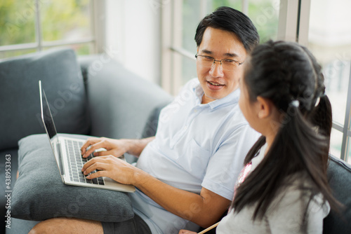 Young Asian love family father and daughter teach homework by computer notebook on sofa in living room at home which smiling and felling happy. live at home concept in COVID-19 situation © linghaa