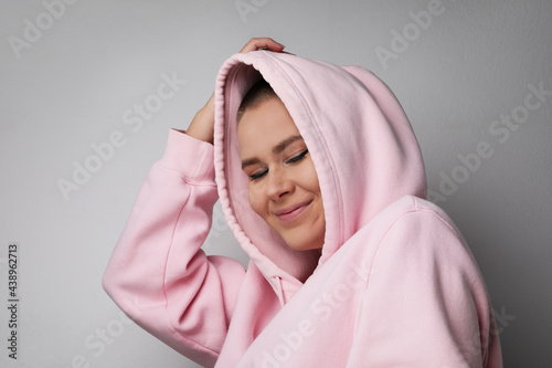 Happy and young woman posing on white wall, pulling the hood over the heads.