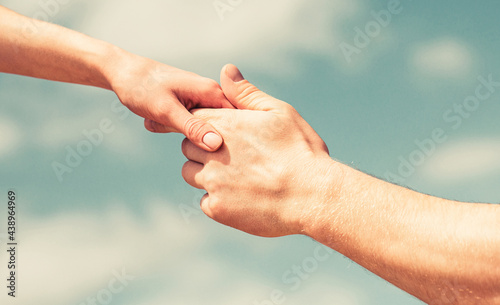 Hands of man and woman reaching to each other, support. Solidarity, compassion, and charity, rescue. Giving a helping hand. Hands of man and woman on blue sky background. Lending a helping hand © Yevhen