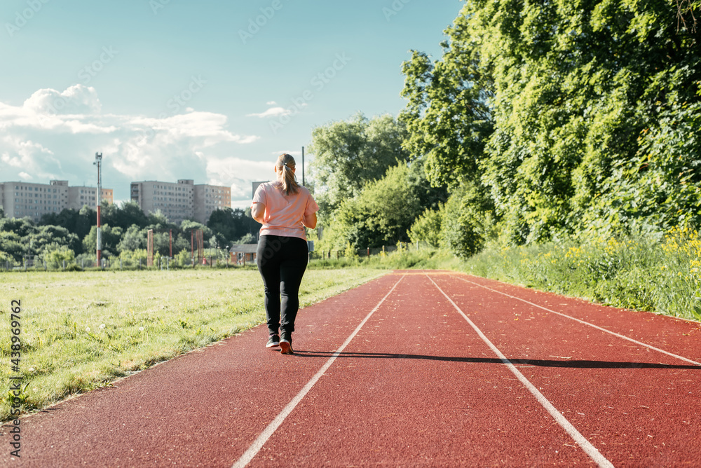 Training at the stadium, outdoors. Young plus size woman walking outside on sunny summer day. Overweight woman doing sports, back view. Active lifestyle, weight loss Training at the stadium, outdoors. Young plus size woman walking outside on sunny summer day. Overweight woman doing sports, back view. Active lifestyle, weight loss
