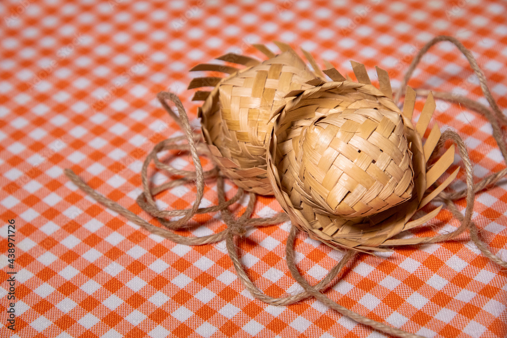 Two straw hat on a orange checkered background and rope. Traditional object used in the June festivities in Brazil. Known as 