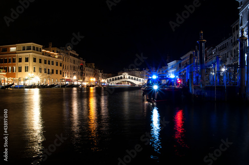 Night view of the main bridge of Venice ("Ponte di Rialto"), with a boat in the frontground and the city lights reflected on the water.