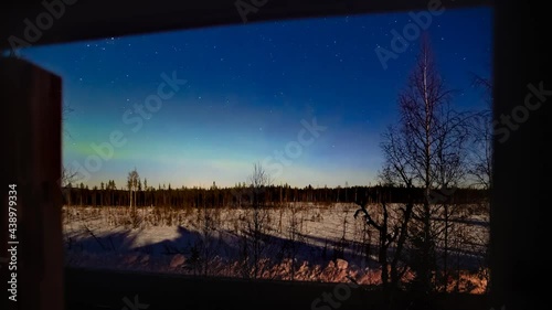 Northern lights until dawn over moonlit winter landscape, shot through a window
