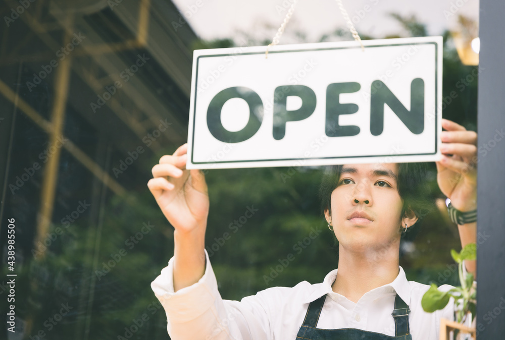 Young asian man Flip the open label to welcome customer and open the coffee shop in morning. Male asian Barista open the coffee cafe at doorway with reflection in mirror. Young asian man Flip the open label to welcome customer and open the coffee shop in morning. Male asian Barista open the coffee cafe at doorway with reflection in mirror.