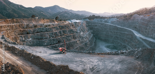 Gravel quarry with terraces, piles of stone and red crusher machine. Panorama with mountains background in twilight photo