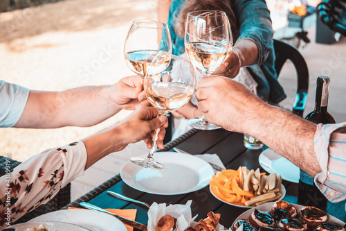 Crop photo of the hands of party of friends on patio over glass of white wine. Joint vacation concept