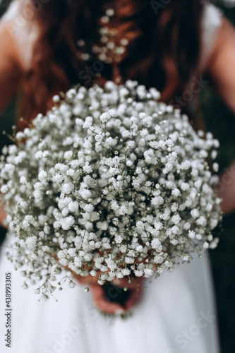 The bride is holding a bouquet of small white flowers. Beautiful wedding bouquet. Morning of the bride.