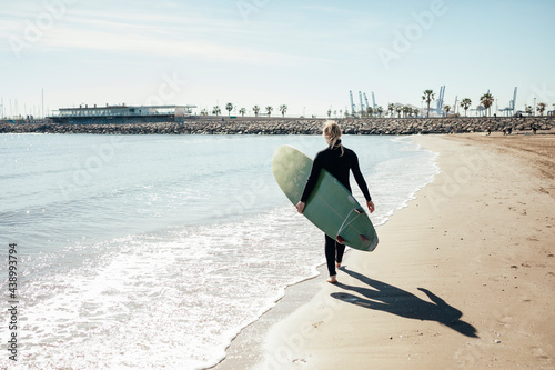 Young girl walking along the shore looking at the ocean with a surfboard. Sports concept.