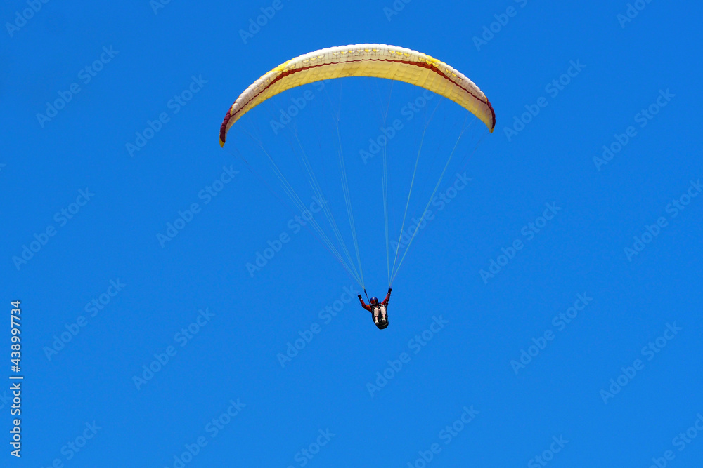The athlete is flying a paraglider. Yellow paraglider against the blue sky on a clear sunny summer day The athlete is flying a paraglider. Yellow paraglider against the blue sky on a clear sunny summer day
