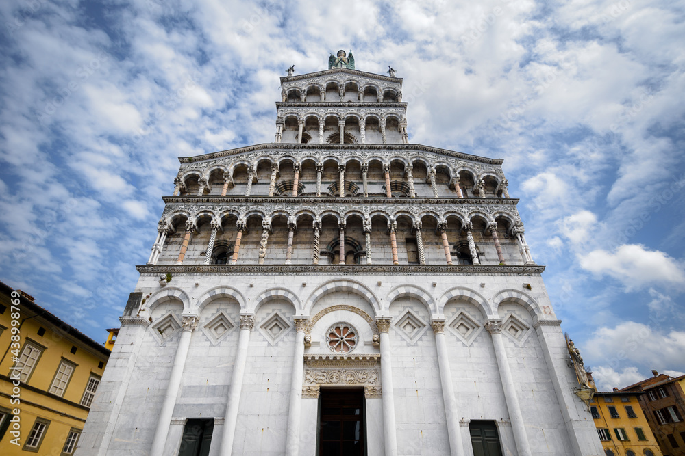 Church and square of San Michele (Saint Michael) in Lucca, Tuscany (Italy). View of the white marble facace, with arches and decorated columns over blue cloudy sky