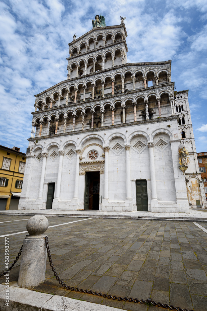 Church and square of San Michele (Saint Michael) in Lucca, Tuscany (Italy). View of the white marble facace, with arches and decorated columns over blue cloudy sky