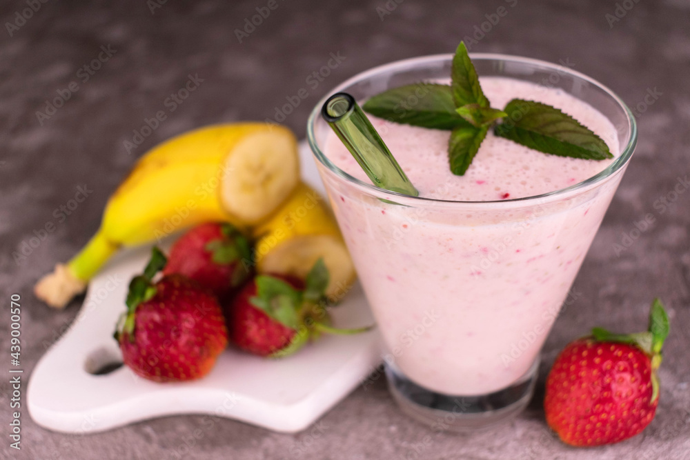 A glass of strawberry banana milkshake on a gray background. A glass of strawberry banana milkshake on a gray background.