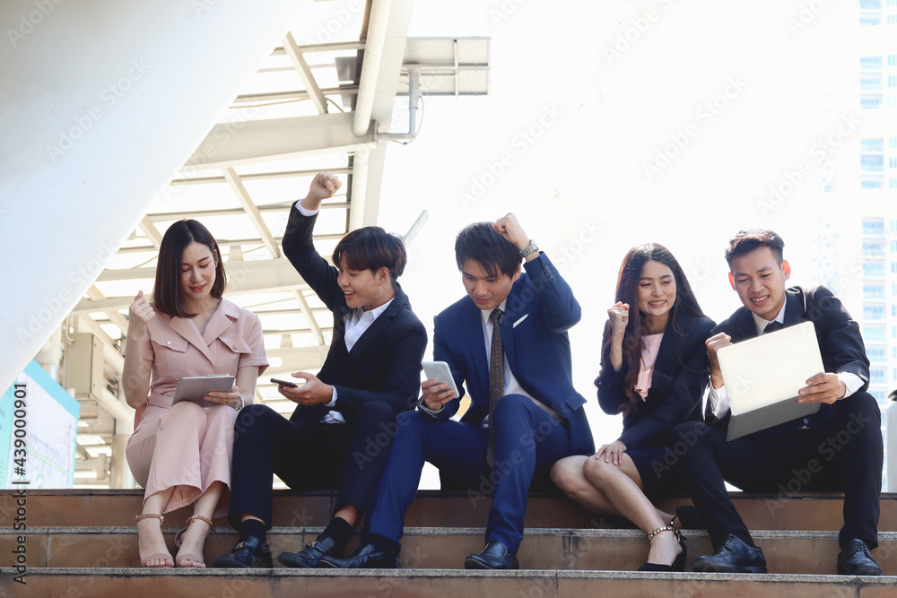 Group of young Asian happy businesspeople socializing while sitting on stairway in modern downtown city. businesspeople talking and having conversations. Group of young Asian happy businesspeople socializing while sitting on stairway in modern downtown city. businesspeople talking and having conversations.