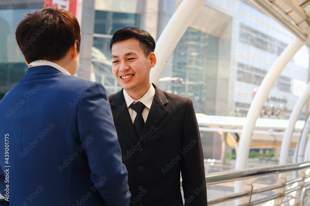 Two successful businessmen in suit talking and discussing at modern city downtown with skyscraper building as blurred background, businesspeople meeting at outside office. Two successful businessmen in suit talking and discussing at modern city downtown with skyscraper building as blurred background, businesspeople meeting at outside office.