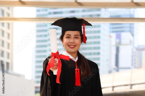 Happy smiling graduated student, young beautiful Asian woman warming square academic hat cap and giving certificate to camera, celebrating successful education on commencement graduation day when fini