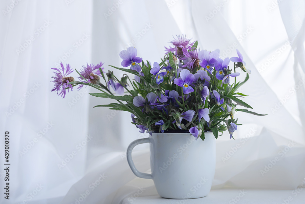 Fototapeta premium Delicate bouquet of flowers pansies in a cup on the windowsill