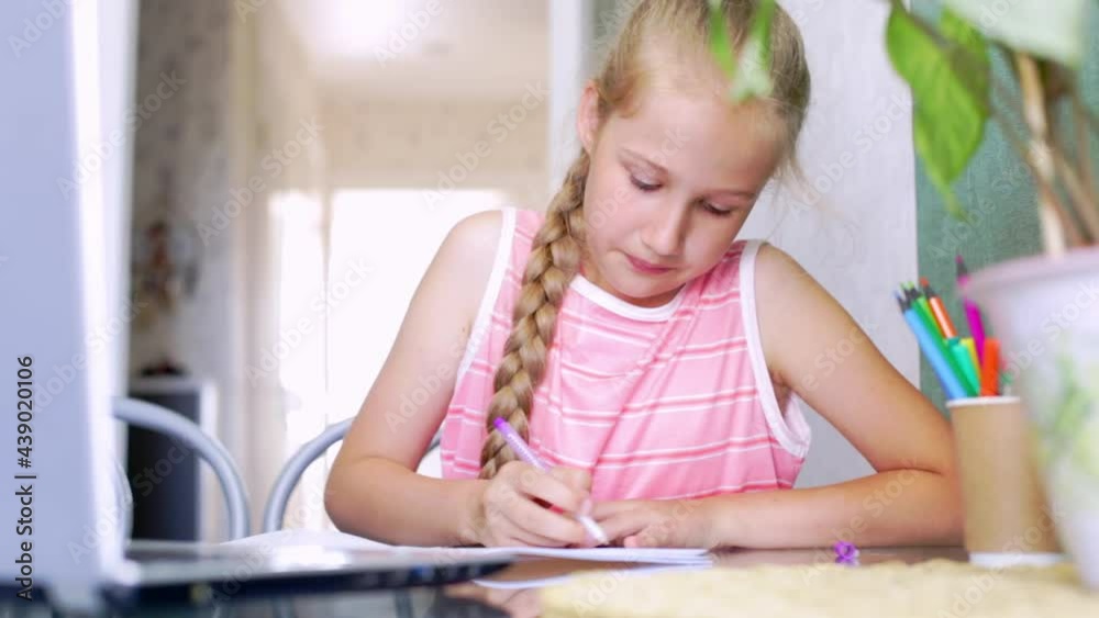 Caucasian girl doing homework at home, writes in a notebook. Schoolgirl speaking emotionally to online teacher, takes a school test online during distance education. Children e-learning concept. Caucasian girl doing homework at home, writes in a notebook. Schoolgirl speaking emotionally to online teacher, takes a school test online during distance education. Children e-learning concept.