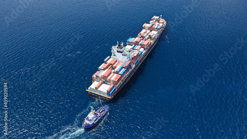 Aerial drone photo of tow - tug boat assisting by pulling or pushing container ship to anchor in terminal port