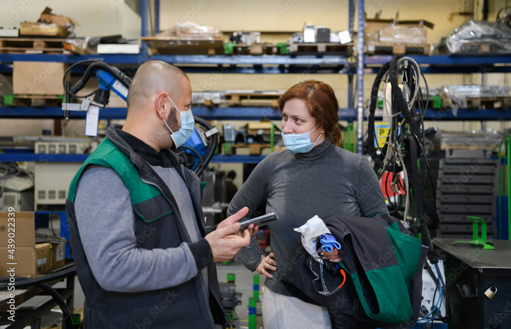 Industrial workers with face masks protected against corona virus discussing about production in factory. People working during COVID-19 pandemic. Industrial workers with face masks protected against corona virus discussing about production in factory. People working during COVID-19 pandemic.