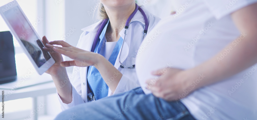 Smiling woman doctor shows pictures on the tablet to pregnant young woman at hospital. Smiling woman doctor shows pictures on the tablet to pregnant young woman at hospital.