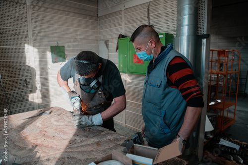 Industrial work during a pandemic. Two men work in a heavy metal factory, wearing a mask on their face due to a coronavirus pandemic