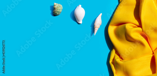 Yellow women's shawl with seashells on blue background. Copy space
