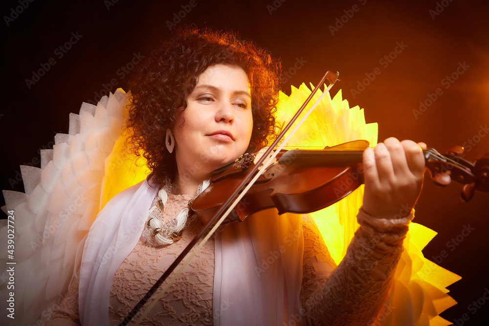 A brunette girl in an elegant dress, with violin and white angel wings ...