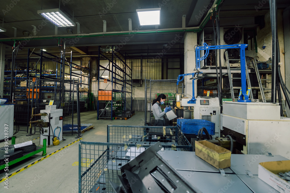 Naklejka premium woman working in the metal industry in the production of new machines wears a face mask during work due to the coronavirus pandemic