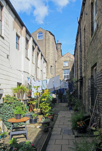 back alley between streets with rows of traditional stone houses in hebden bridge west yorkshire with washing drying on lines and pot plants in bright summer sunshine