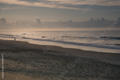 Fototapeta Naklejka Na Ścianę i Meble -  Beautiful early morning almost deserted beach. One person and one dog enjoying the peaceful solitude of the rhythmic waves.