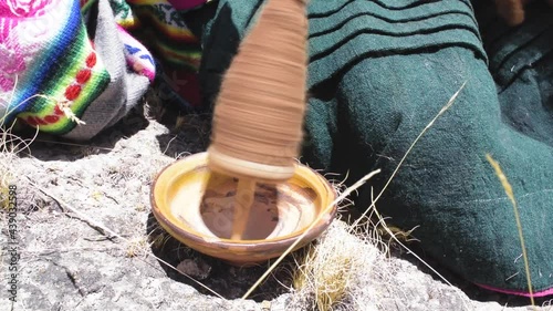 Andean woman spinning alpaca fiber by hand surrounded by an Andean landscape of Peru