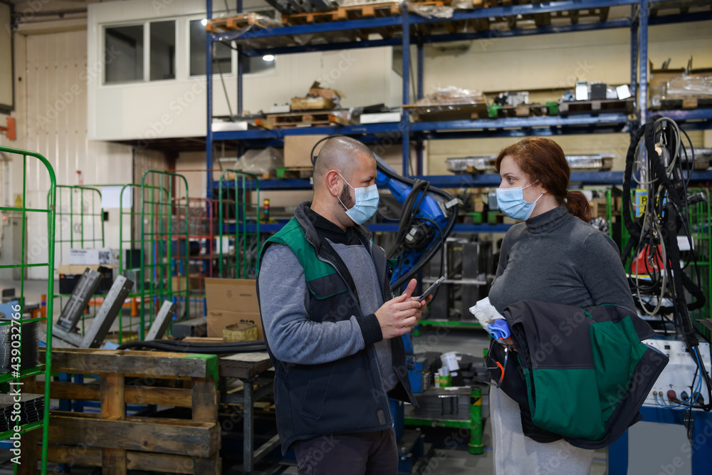 Industrial workers with face masks protected against corona virus discussing about production in factory. People working during COVID-19 pandemic.