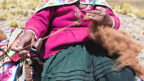 Andean woman spinning alpaca fiber by hand surrounded by an Andean landscape of Peru photo