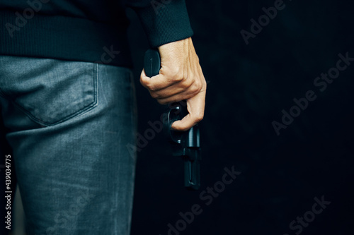 Dangerous pistol in person hand. Man in sweater and jeans is holding gun. Criminal with revolver on black background. Firearms for shooting.