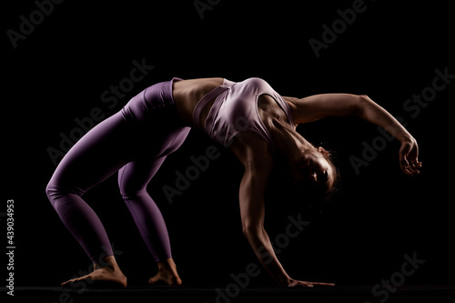 Fit girl practicing yoga in a studio. Half silhouette side lit fitness model...