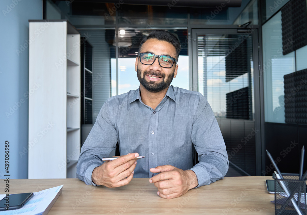 Smiling indian businessman in glasses talking to camera at work by video  call conference. Financial advisor executive consulting client remotely  online in modern office looking at camera. Webcam view Stock 写真