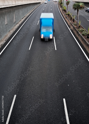 A blue lorry / mini truck in movement on a black asplalt road, light trails and intentional movement/zoom effect.