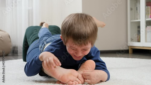 Laughing little boy playing with mother on floor and tickling her bare feet. Family having fun and playing together