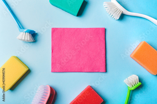 House cleaning product and empty pink napkin in center, blue background, copy space. Flat lay or top view. Cleaning service or housekeeping concept with space for text or design in center