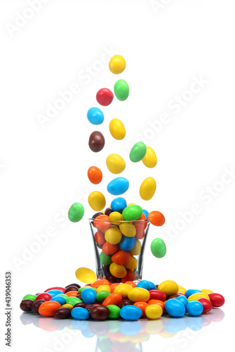Fotografía caramelos de chocolates recubiertos de colores cayendo hacia un vaso