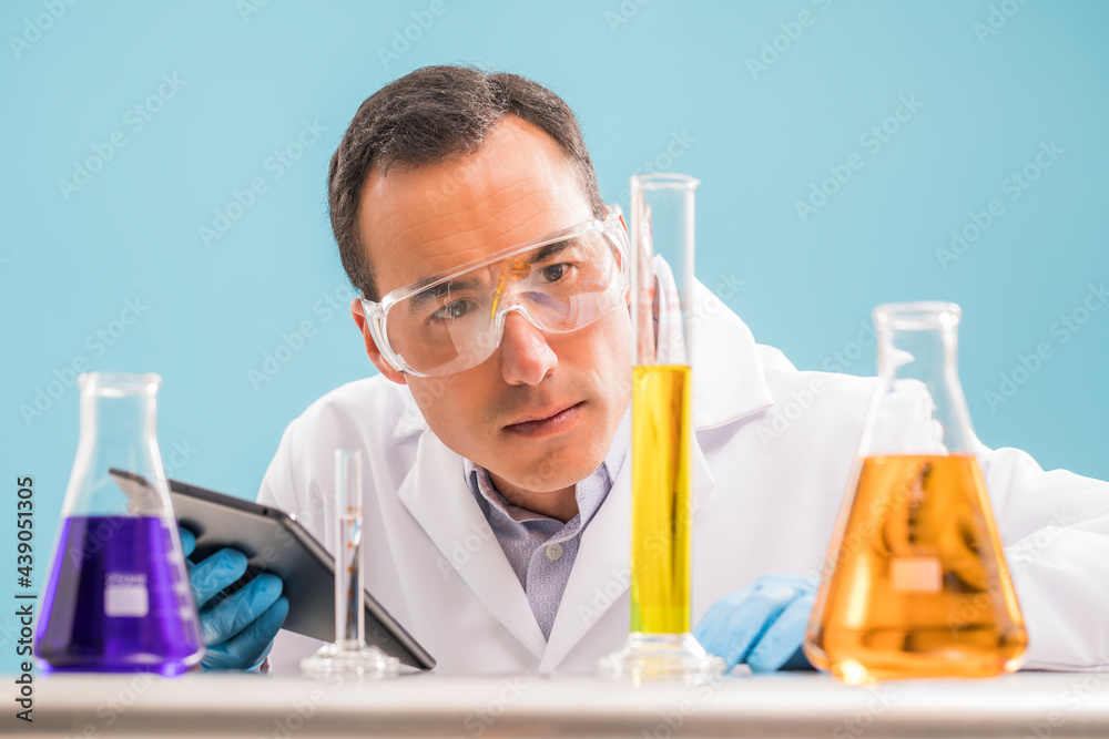 Scientist with digital tablet looking at yellow liquid in measuring beaker Scientist with digital tablet looking at yellow liquid in measuring beaker