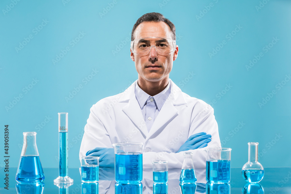 Portrait of scientist with beakers with blue liquid in foreground Portrait of scientist with beakers with blue liquid in foreground