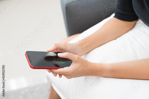 Close up of woman hand using smartphone, browsing internet, checking social media, sitting on the sofa in living room.