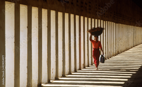 Myanmar, Bagan, Mandalay Division, Woman walking in portico of Schwezigon Pagoda carrying wood on her head photo