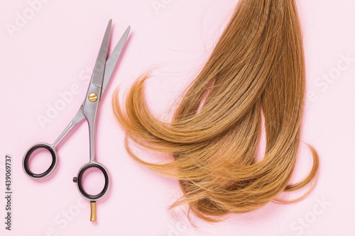 Children's strand of hair and scissors on a pink background, top view