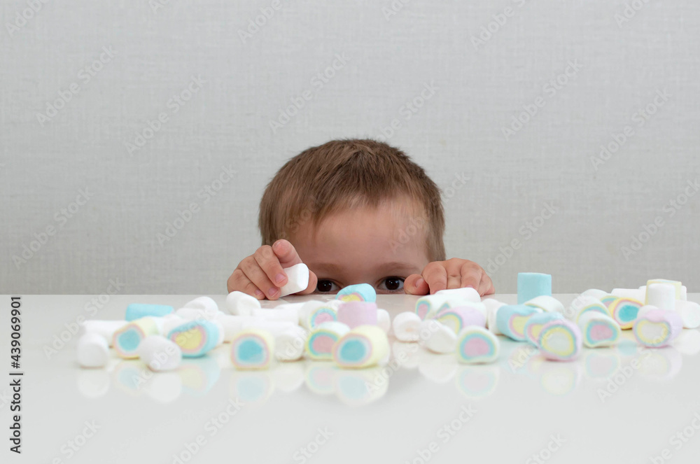 Big baby eyes in front of marshmallow, colored marshmallow. The child is addicted to sugar. The problem of baby food. Selective Focus Big baby eyes in front of marshmallow, colored marshmallow. The child is addicted to sugar. The problem of baby food. Selective Focus