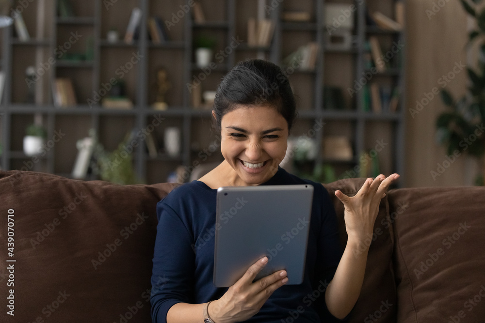 Fototapeta premium It is amazing. Emotional young lady of indian ethnicity splash hand wow look on digital tablet screen excited with great sales proposition. Euphoric teen female student get email with good exam result