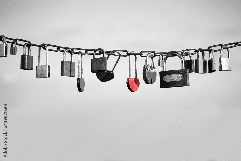 Love padlocks on a chain on a light grey background. Diverse locks with one colored in red as a symbol of unique feelings of each love story.